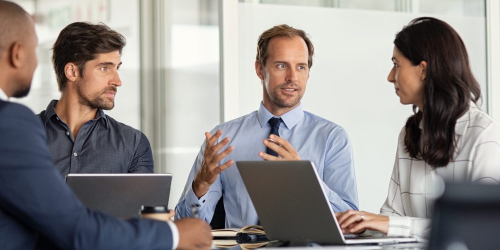 Businessman giving some new ideas about project to his partners in conference room. Mature leader discussing over new business plans in office with his employees. A group of businessmen and businesswoman talking during meeting.