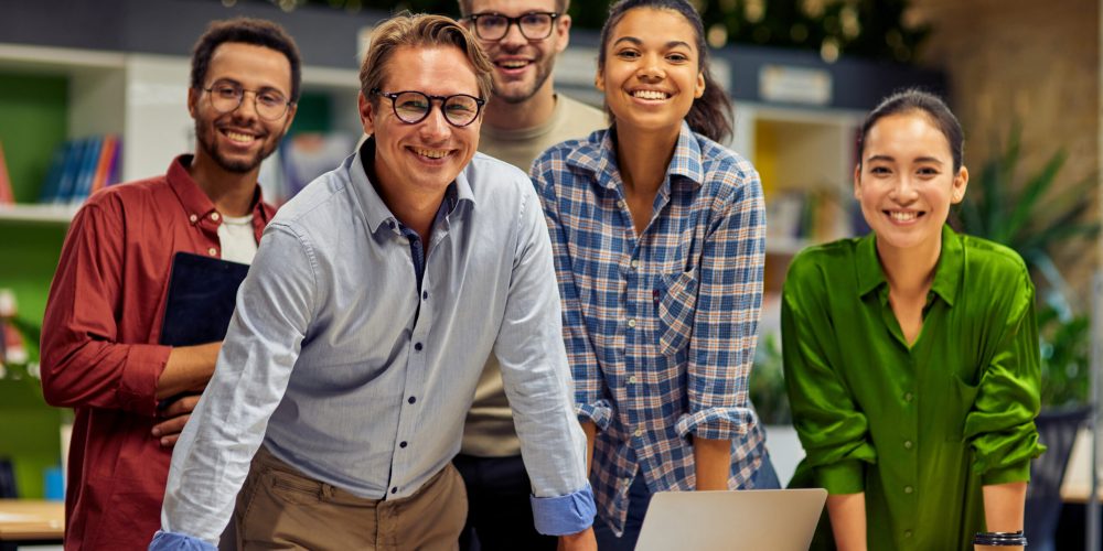 Working as a team. Group of young successful multi ethnic business team looking at camera and smiling while having a meeting in the modern office and coworking space. Business, teamwork, cooperation